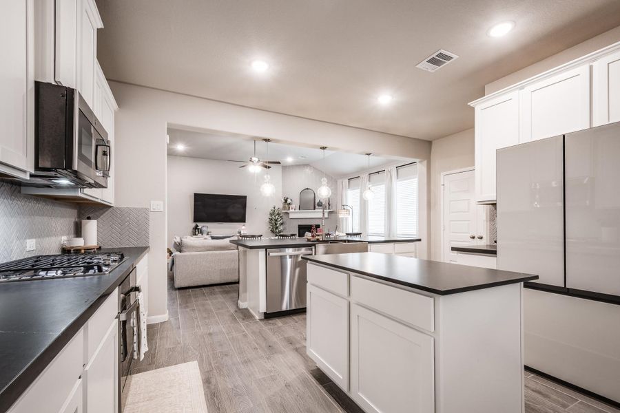 This modern kitchen features sleek white cabinetry, dark countertops, and a central island. It opens to a cozy living area with a mounted TV and ample natural light from large windows, creating a spacious and inviting atmosphere. This modern kitchen features sleek white cabinetry, dark countertops, and a central island. It opens to a cozy living area with a mounted TV and ample natural light from large windows, creating a spacious and inviting atmosphere.