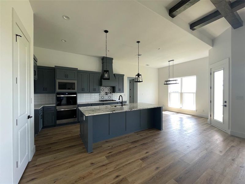 Kitchen with decorative backsplash, stainless steel appliances, light stone countertops, dark wood-style floors, and a center island with sink Kitchen with decorative backsplash, stainless steel appliances, light stone countertops, dark wood-style floors, and a center island with sink