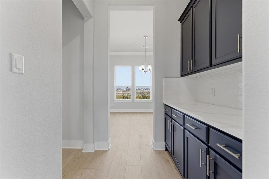 Bar area featuring light stone countertops, crown molding, pendant lighting, light wood-style floors, and a chandelier