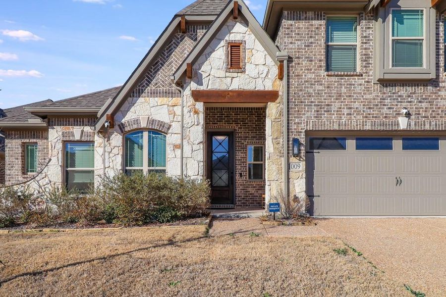 French country inspired facade featuring stone siding, an attached garage, driveway, brick siding, and a shingled roof