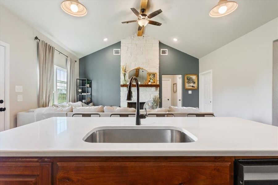 Kitchen featuring brown cabinetry, open floor plan, a ceiling fan, beamed ceiling, and a kitchen island with sink