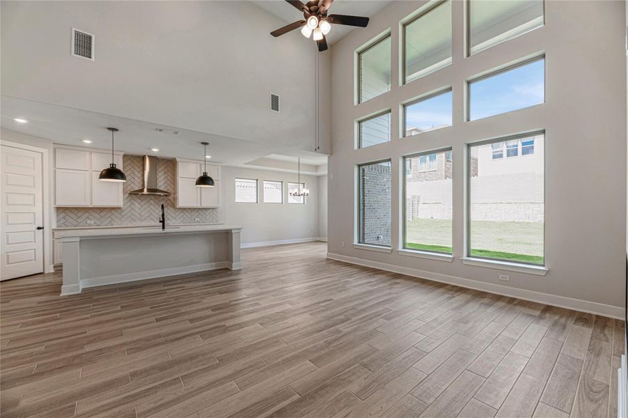Unfurnished living room featuring a towering ceiling, light wood finished floors, and ceiling fan