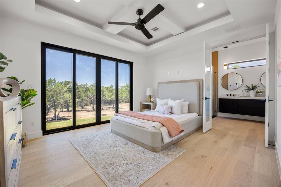 A spacious bedroom retreat offers wood floors, a tray ceiling, and a full-length sliding glass door opening to tranquil views.