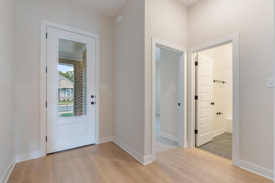 Entryway featuring a partially glass-paneled door with dark hardware, wood-finish flooring, and crisp white trim