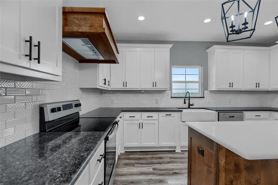 Kitchen with light hardwood / wood-style flooring, tasteful backsplash, premium range hood, sink, and appliances with stainless steel finishes