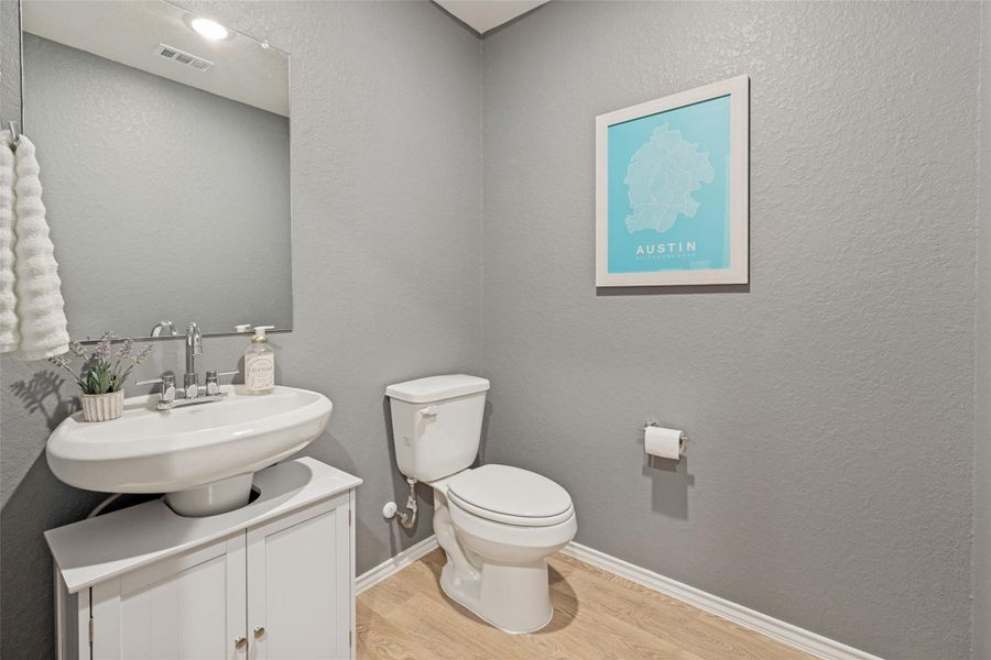 A compact and functional bathroom features a sleek pedestal sink and wood-look flooring.