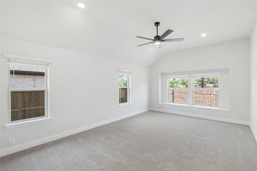 Empty bedroom with vaulted ceiling, ceiling fan, carpet flooring, and three windows
