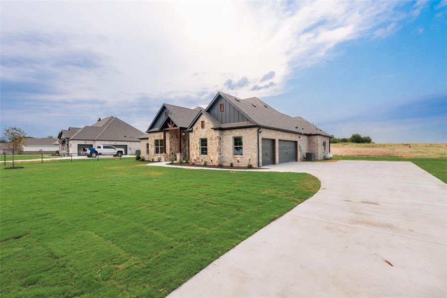 View of front of property with concrete driveway, a front lawn, board and batten siding, stone siding, and a garage View of front of property with concrete driveway, a front lawn, board and batten siding, stone siding, and a garage