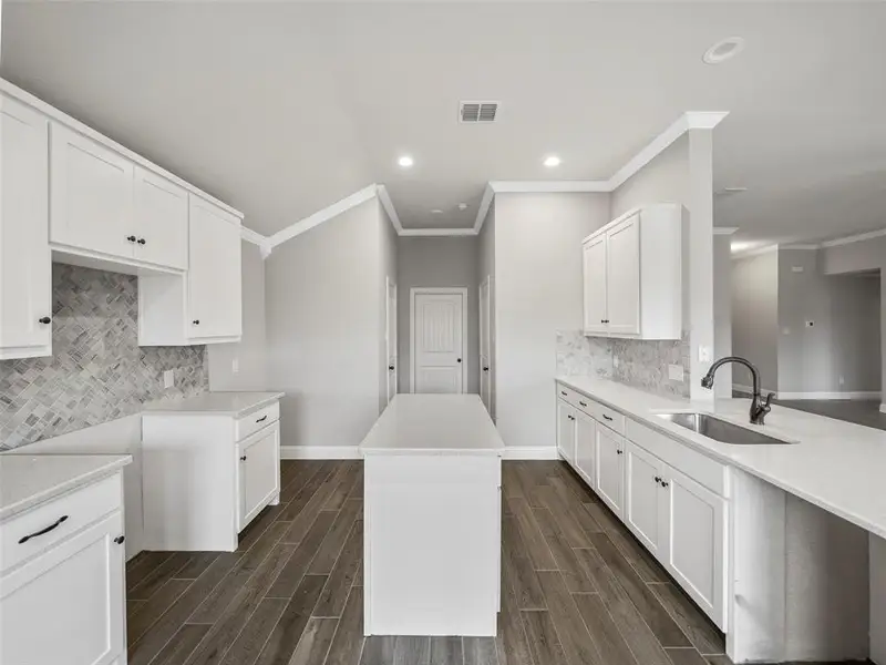 Kitchen featuring visible vents, a sink, crown molding, baseboards, and decorative backsplash