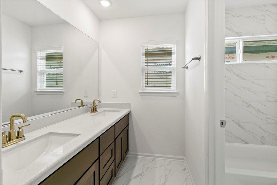 Luxurious secondary bathroom featuring sleek dual sinks, elegant fixtures, and beautiful tile flooring for a modern touch.