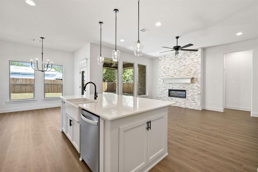 Kitchen featuring white cabinetry, a center island with sink, dishwasher, a fireplace, and light stone countertops