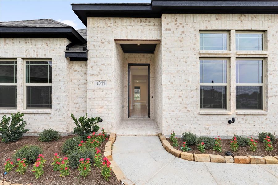 Home entrance with light brick exterior, recessed front door, and landscaped flower beds with red blooms Home entrance with light brick exterior, recessed front door, and landscaped flower beds with red blooms