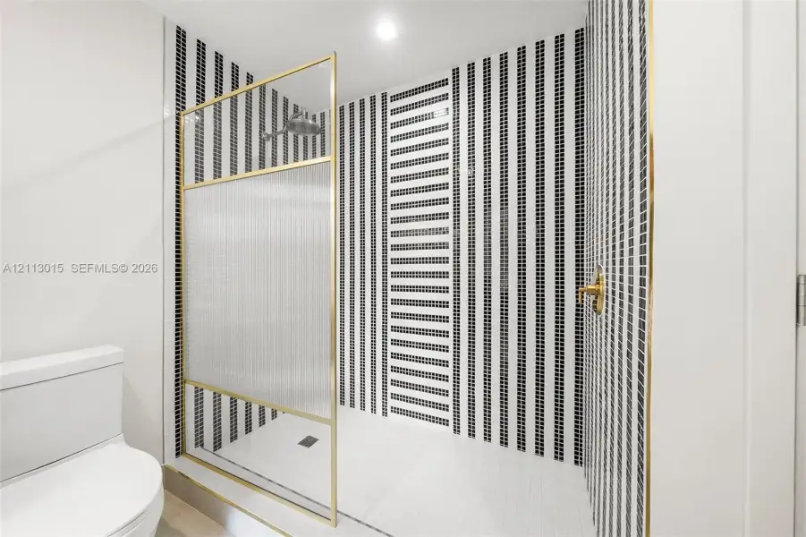 Walk-in shower featuring a brass-framed glass enclosure, floor-to-ceiling vertically striped mosaic tile work, and gold-finish plumbing fixtures