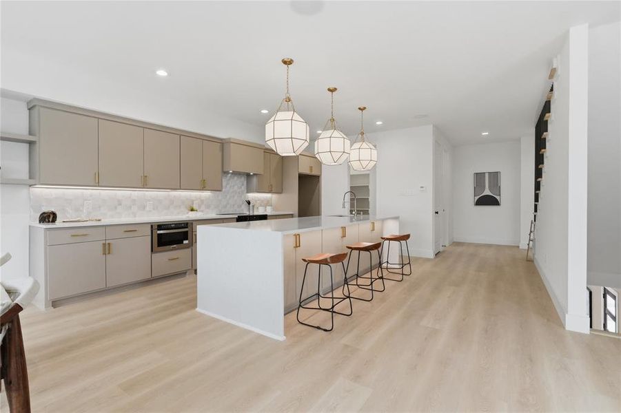 Spacious kitchen featuring an expansive island with seating, a built-in microwave, light-toned cabinetry, light wood-finish flooring, and a patterned tile backsplash Spacious kitchen featuring an expansive island with seating, a built-in microwave, light-toned cabinetry, light wood-finish flooring, and a patterned tile backsplash