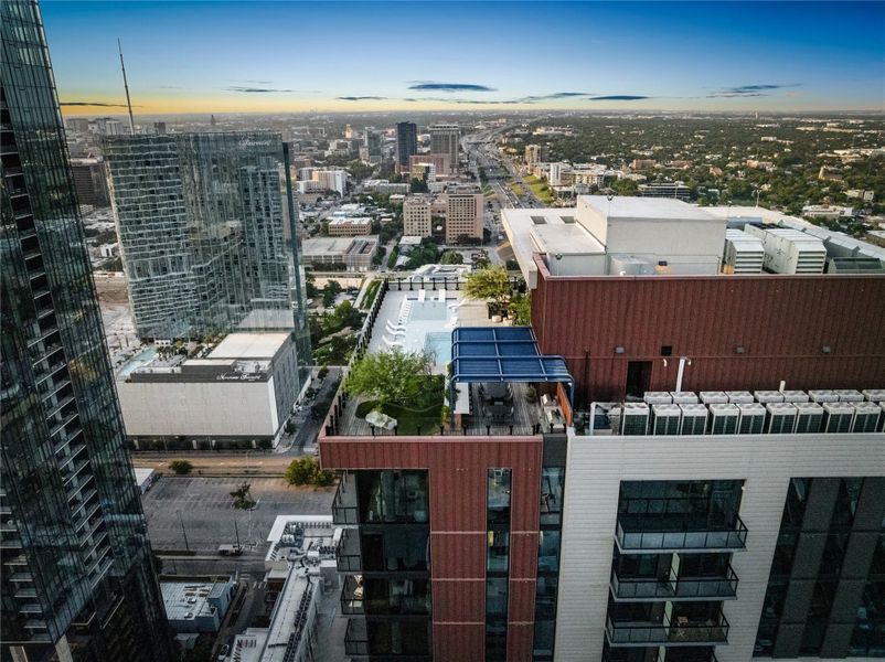 An aerial perspective reveals a rooftop pool deck with urban city views and distant highways.