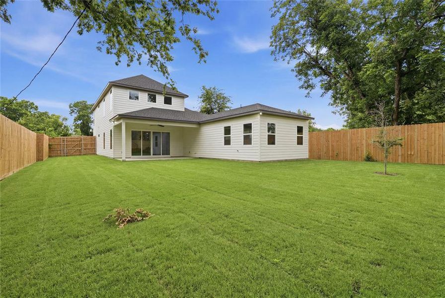 Expansive backyard featuring a manicured lawn, full perimeter fencing, and a covered patio with sliding glass doors Expansive backyard featuring a manicured lawn, full perimeter fencing, and a covered patio with sliding glass doors