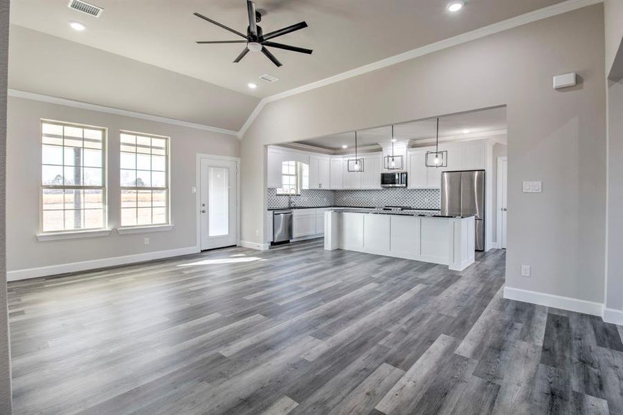 Kitchen view with open floor plan, dark countertops, lofted ceiling, white cabinets, and crown molding