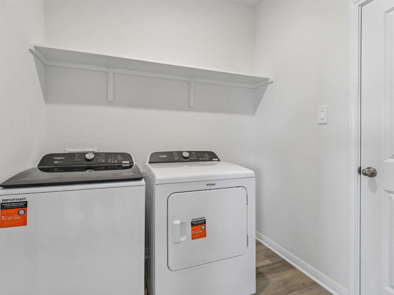 Functional laundry space features overhead shelving and durable wood-look flooring.