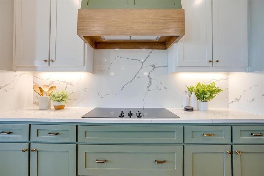 Kitchen featuring premium range hood, black electric cooktop, light stone counters, and tasteful backsplash