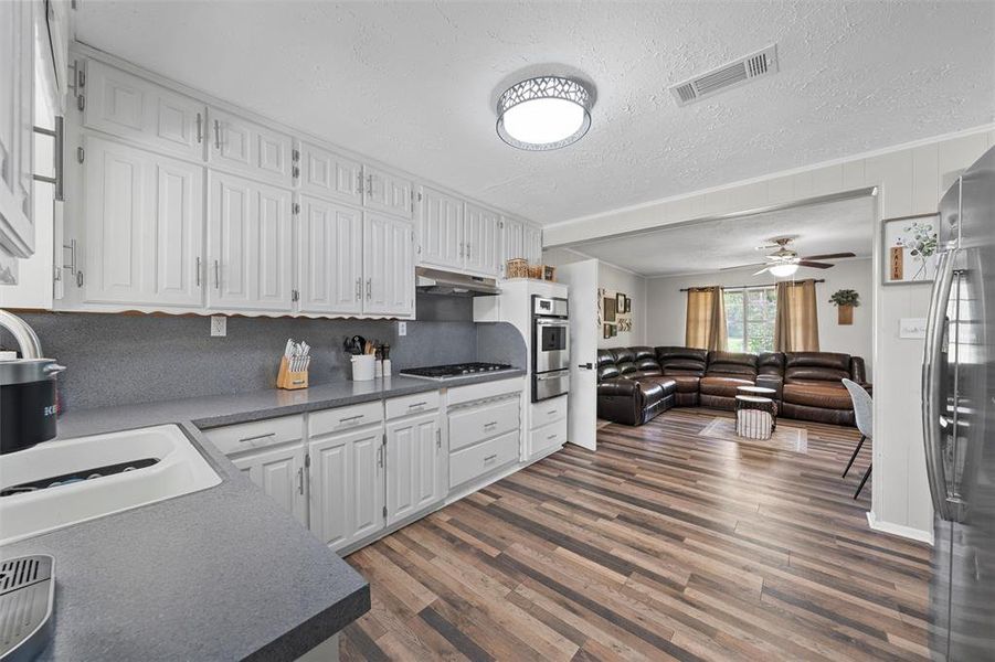 Kitchen with white cabinetry, wood finished floors, stainless steel appliances, a textured ceiling, and dark countertops Kitchen with white cabinetry, wood finished floors, stainless steel appliances, a textured ceiling, and dark countertops