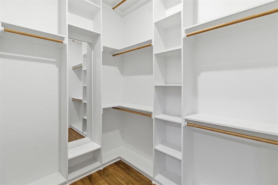 Walk-in closet featuring built-in white shelving, multiple hanging rods, corner shelving units, a full-length mirror, and wood-finish flooring