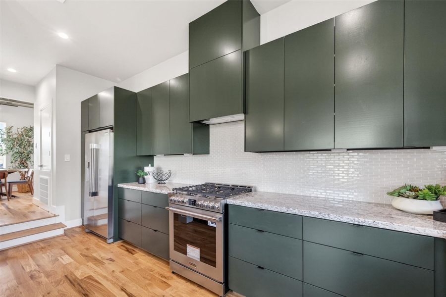 The gas range and ventilation hood take center stage in this view, framed by the home's signature dark cabinetry and tile backsplash. A pantry just off the kitchen provides additional storage, a practical touch for the serious home cook.
