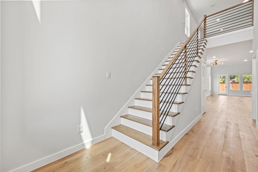 Stairway with light hardwood / wood-style floors, an inviting chandelier, and a high ceiling