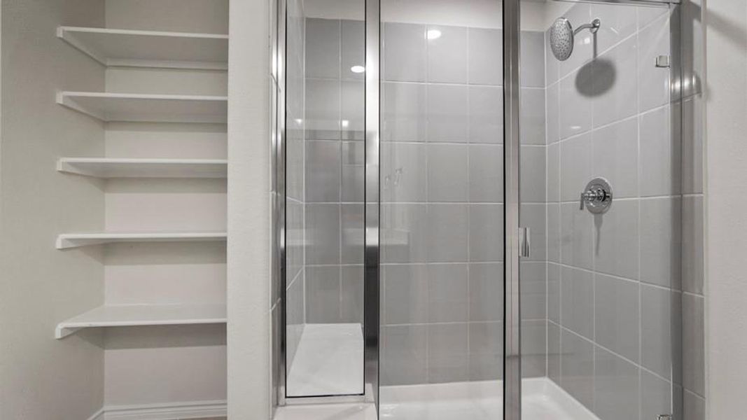 Glass-enclosed shower with subway tile surround, chrome fixtures, and adjacent built-in shelving