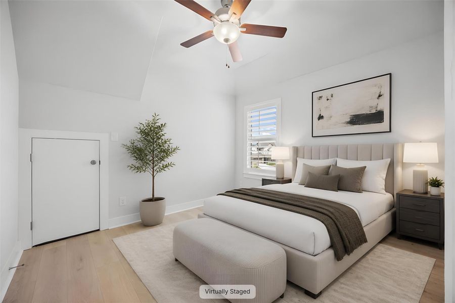 A tranquil bedroom retreat features a ceiling fan, light wood flooring, and a sun-filled window with crisp white blinds.