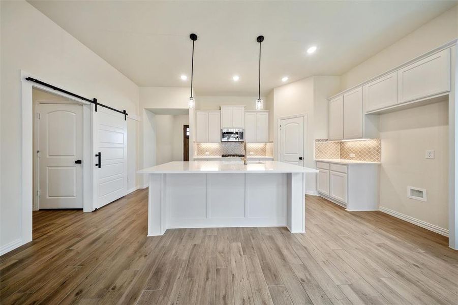 Kitchen featuring a barn door, white cabinetry, backsplash, and recessed lighting