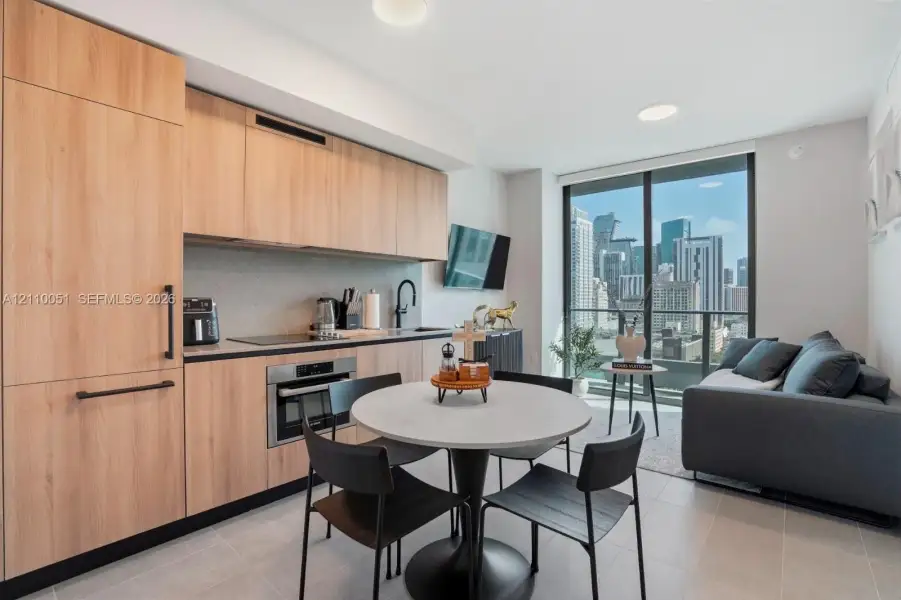 Kitchen featuring custom light-toned cabinetry, built-in panel-ready appliances, quartz countertops, and floor-to-ceiling glass sliding doors with an urban skyline backdrop