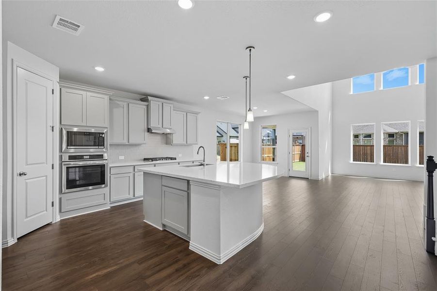 Kitchen with stainless steel appliances, dark wood-style floors, an island with sink, backsplash, and hanging light fixtures Kitchen with stainless steel appliances, dark wood-style floors, an island with sink, backsplash, and hanging light fixtures