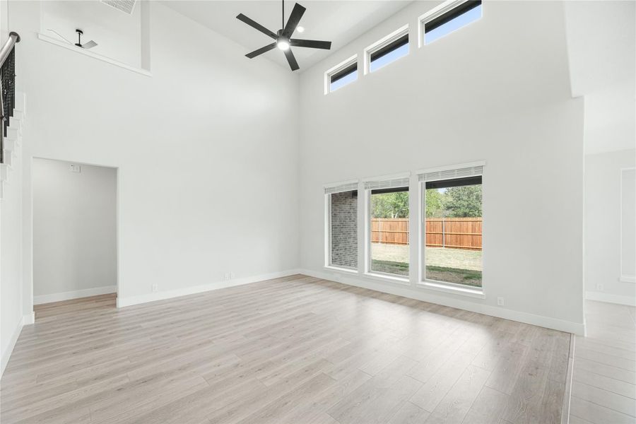 Open living room with two-story ceiling, ceiling fan, light wood floors, and large backyard-facing windows