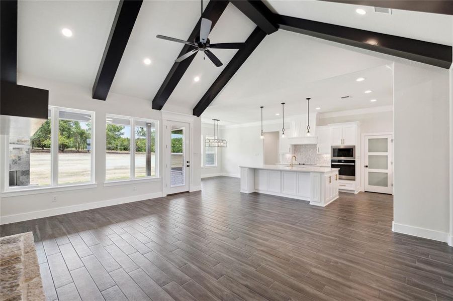 Unfurnished living room featuring beam ceiling, dark wood-type flooring, ceiling fan, sink, and high vaulted ceiling