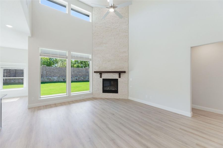 Open living room with two-story ceiling, floor-to-ceiling stone fireplace, and light hardwood floors