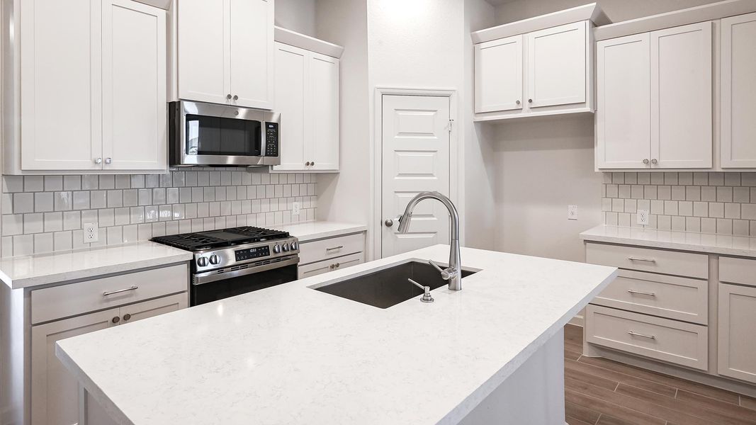 Kitchen featuring backsplash, stainless steel appliances, wood finish floors, a kitchen island with sink, and white cabinets