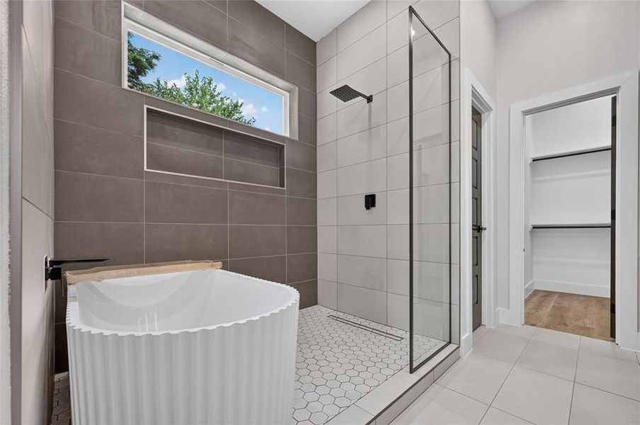 Contemporary bathroom featuring a freestanding soaking tub with a matte black wall-mounted faucet, a walk-in shower with a frameless glass enclosure and matte black fixtures, a recessed shower niche, and hexagonal tile flooring Contemporary bathroom featuring a freestanding soaking tub with a matte black wall-mounted faucet, a walk-in shower with a frameless glass enclosure and matte black fixtures, a recessed shower niche, and hexagonal tile flooring