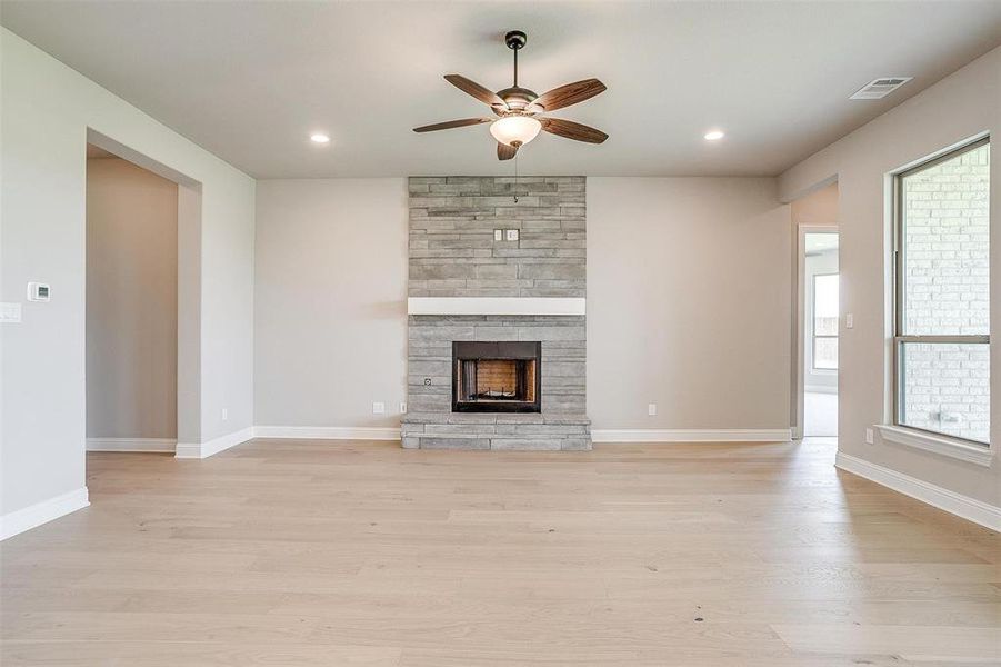 Unfurnished living room featuring ceiling fan, a stone fireplace, and light wood-type flooring