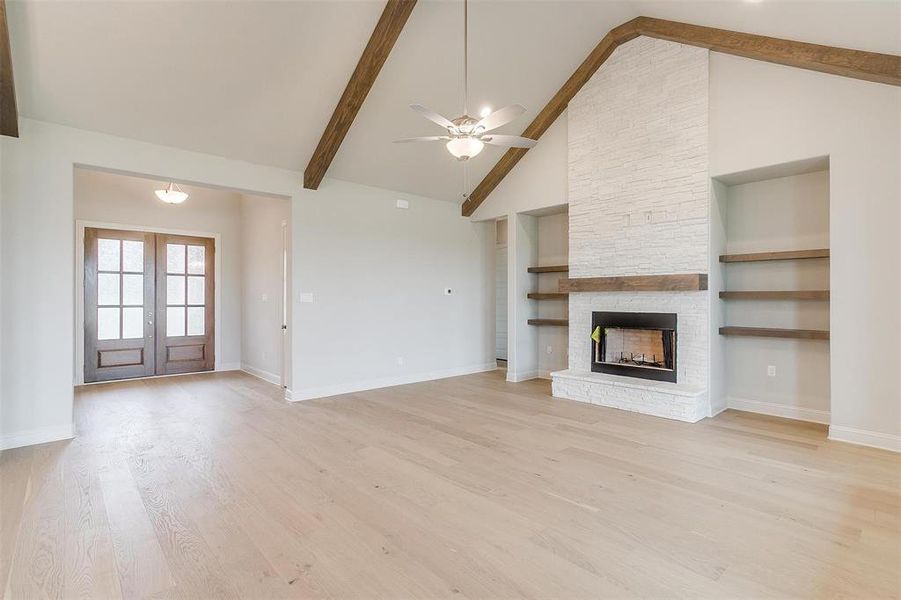 Unfurnished living room featuring a stone fireplace, built in shelves, light hardwood / wood-style flooring, and ceiling fan