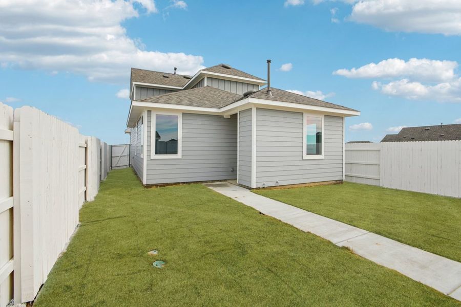 image of the back exterior of a grey two story house with a green grass backyard, a white fence and a blue sky in the background image of the back exterior of a grey two story house with a green grass backyard, a white fence and a blue sky in the background