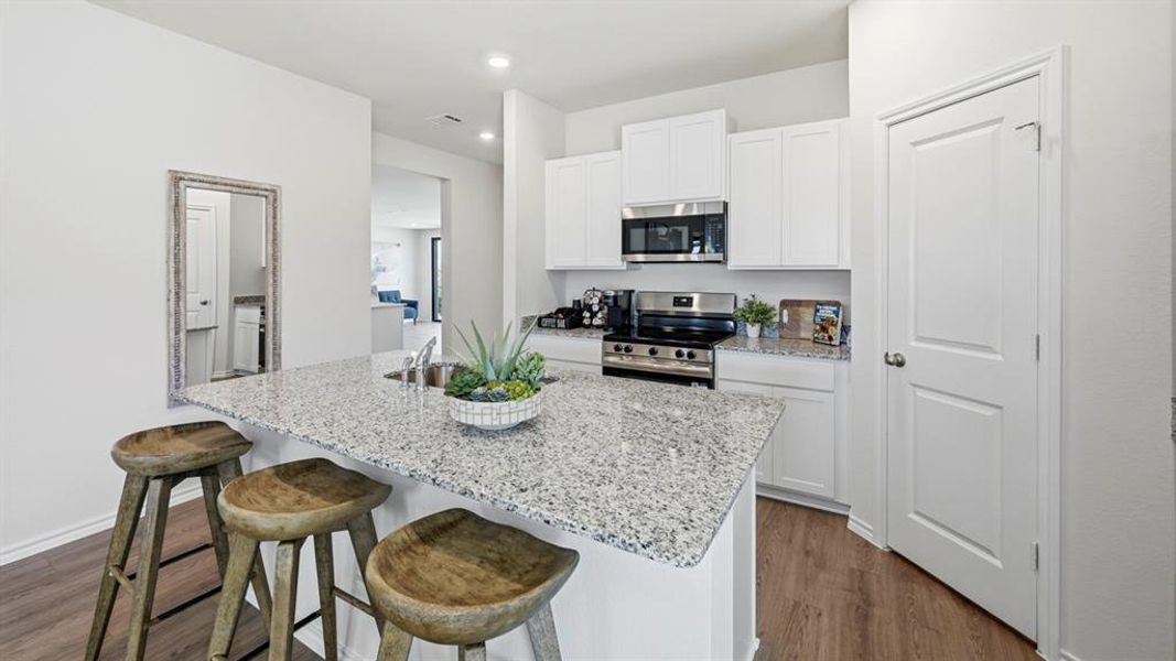 The kitchen features an island with a speckled countertop and an undermount sink, white cabinetry, a stainless steel microwave, and a stainless steel range