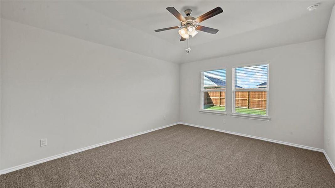 Empty room featuring dark carpet, ceiling fan, and lofted ceiling