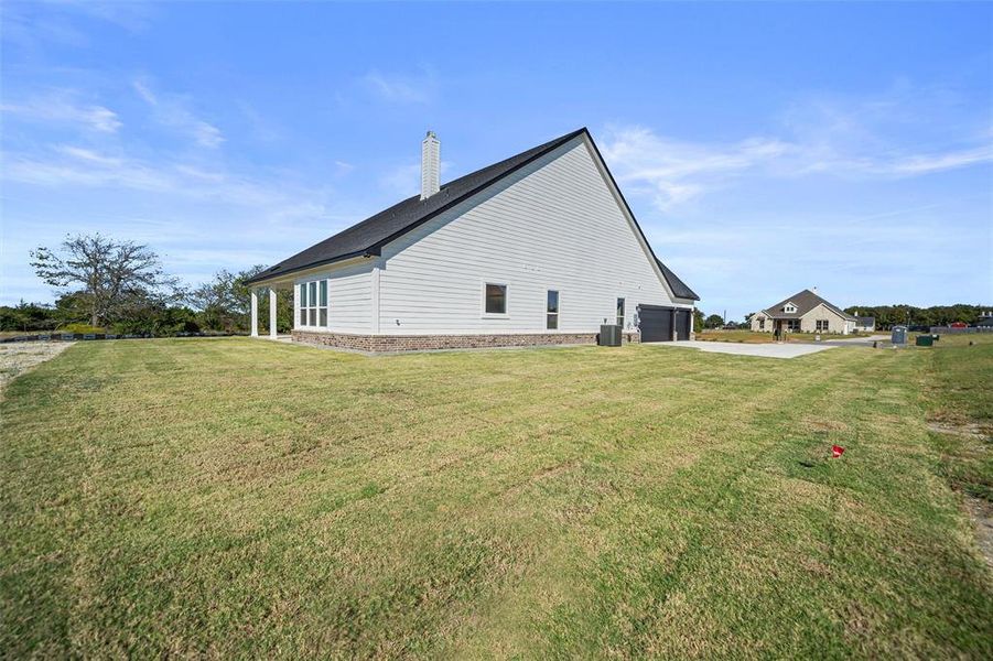 View of property exterior featuring a lawn, a garage, a chimney, and concrete driveway