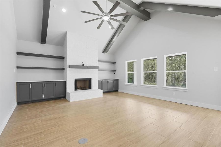 Unfurnished living room with high vaulted ceiling, beam ceiling, ceiling fan, wood finish floors, and a fireplace Unfurnished living room with high vaulted ceiling, beam ceiling, ceiling fan, wood finish floors, and a fireplace