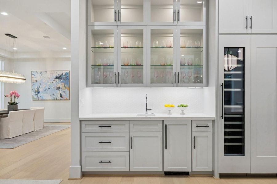 Fabulous Wet-Bar with a JennAir Panel Ready Ice Maker, Slab Quartz Counter, 1.5 Hex Mosaic Glossy Tile Backsplash, Undermount Bar Sink with Single Lever Pull-Down Faucet, and Under-Cabinet Lighting. Glass Fronted Cabinet Doors with Glass Shelving and lighting to display Glasses and Barware.