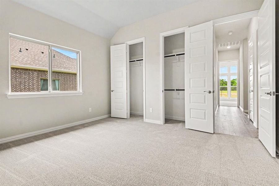Expansive room featuring light neutral carpeting, a large window, and two built-in closets with bi-fold doors Expansive room featuring light neutral carpeting, a large window, and two built-in closets with bi-fold doors