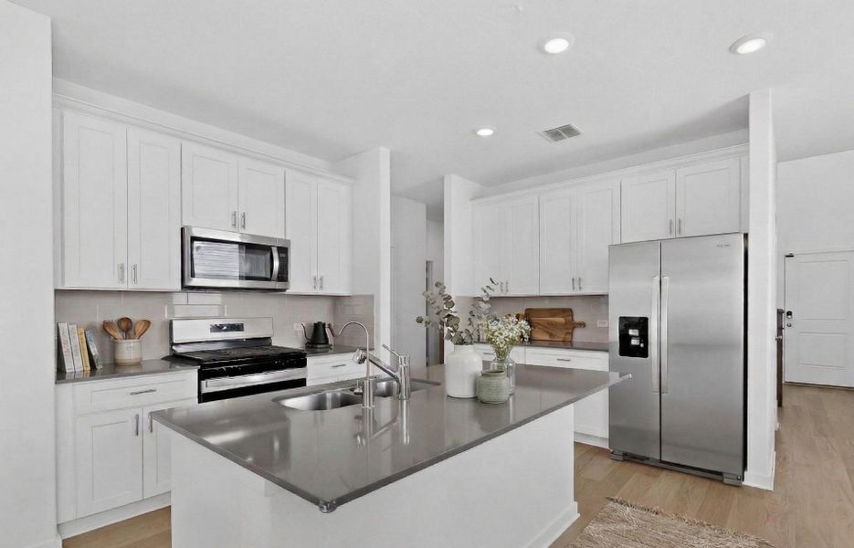 Kitchen featuring stainless steel appliances, white cabinetry, light wood finished floors, an island with sink, and tasteful backsplash