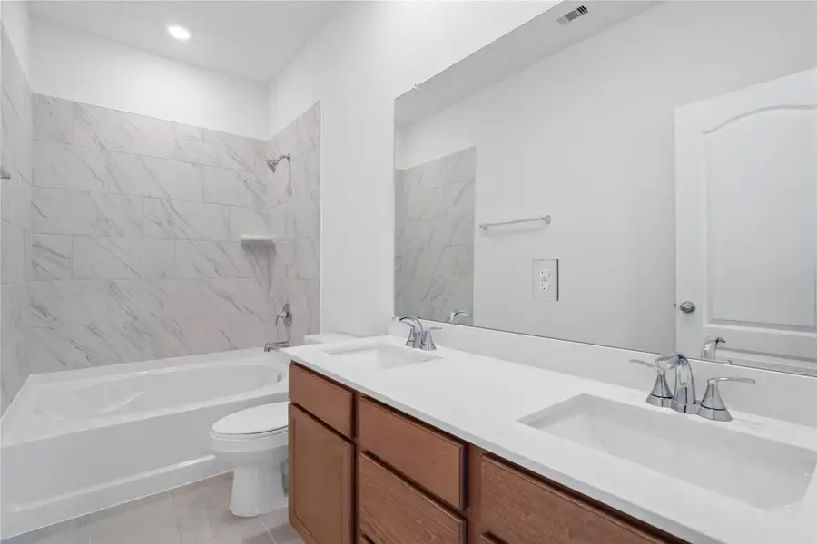 This move-in ready primary bathroom offers a spacious tub/shower combination with a tiled surround, stained cabinetry topped with light countertops, dual sinks, high ceilings, neutral paint, a large mirror, and sleek, modern finishes for a polished look. This move-in ready primary bathroom offers a spacious tub/shower combination with a tiled surround, stained cabinetry topped with light countertops, dual sinks, high ceilings, neutral paint, a large mirror, and sleek, modern finishes for a polished look.