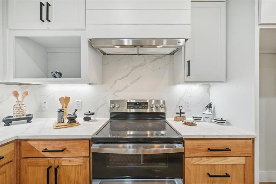 Kitchen featuring electric range, light stone counters, white cabinetry, and extractor fan