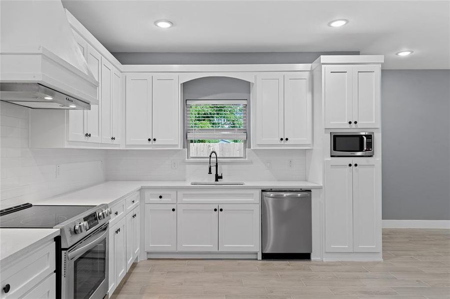 Kitchen featuring stainless steel appliances, white cabinets, custom exhaust hood, decorative backsplash, and recessed lighting Kitchen featuring stainless steel appliances, white cabinets, custom exhaust hood, decorative backsplash, and recessed lighting